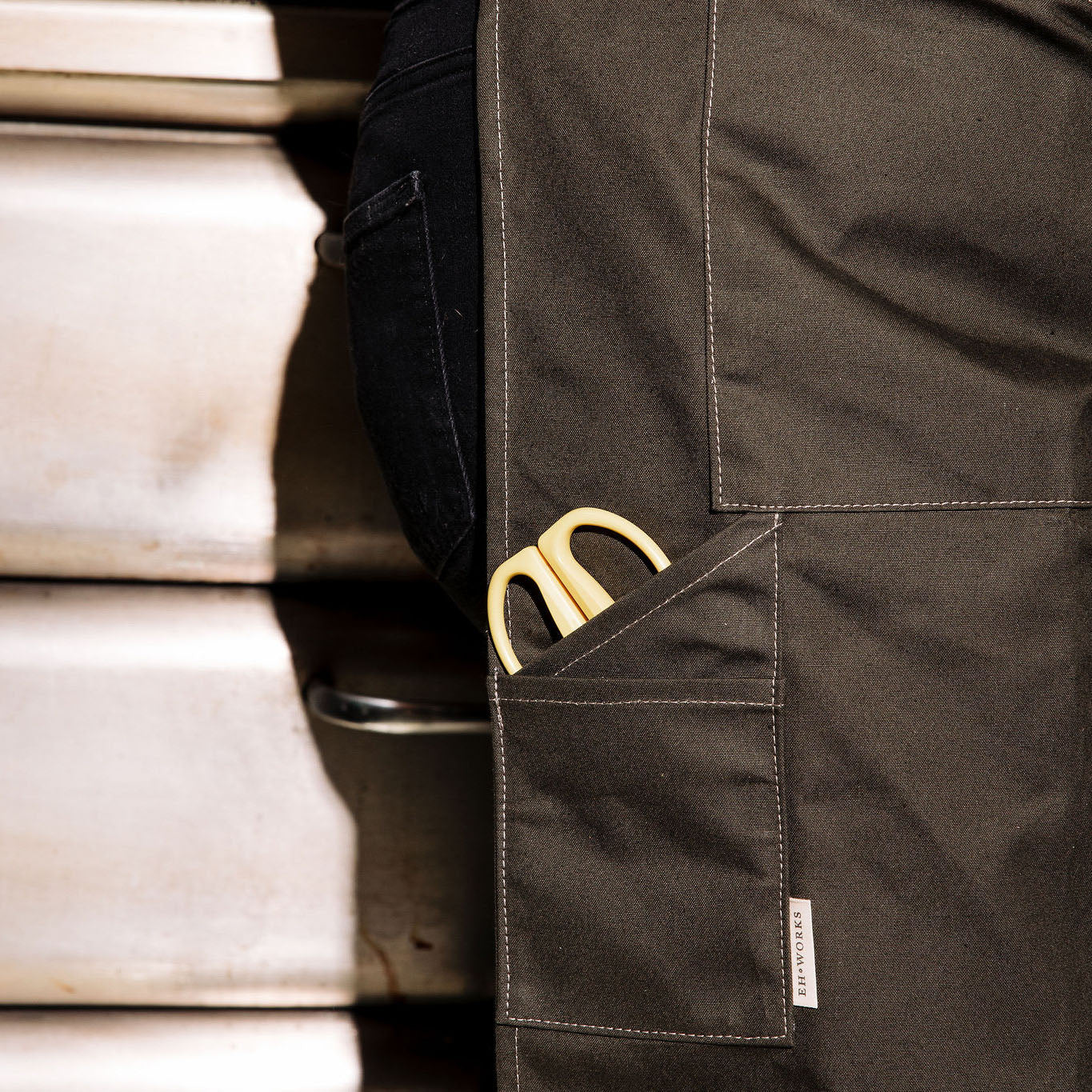 Yellow-handled scissors tucked into the front pocket of a pine canvas apron with the EH·Works label