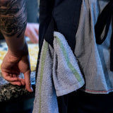 Close-up of a navy canvas apron waistband with a striped kitchen towel tucked into the strap