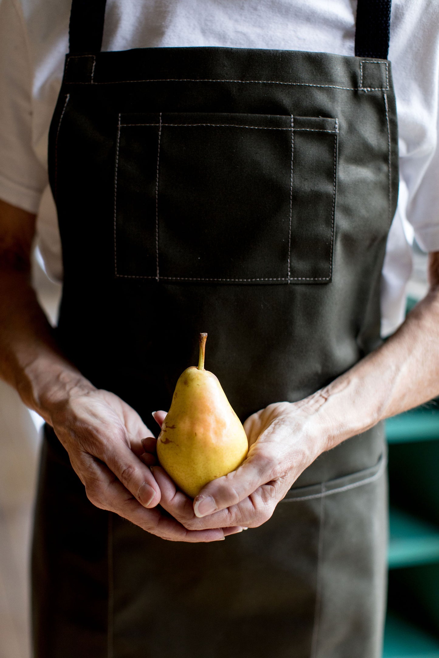  Person wearing a pine canvas apron with a front pocket, holding a pear in both hands