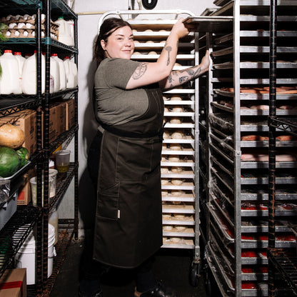  Person wearing a pine canvas apron while sliding a baking tray into a rack in a walk-in cooler