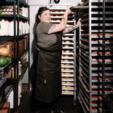  Person wearing a pine canvas apron while sliding a baking tray into a rack in a walk-in cooler
