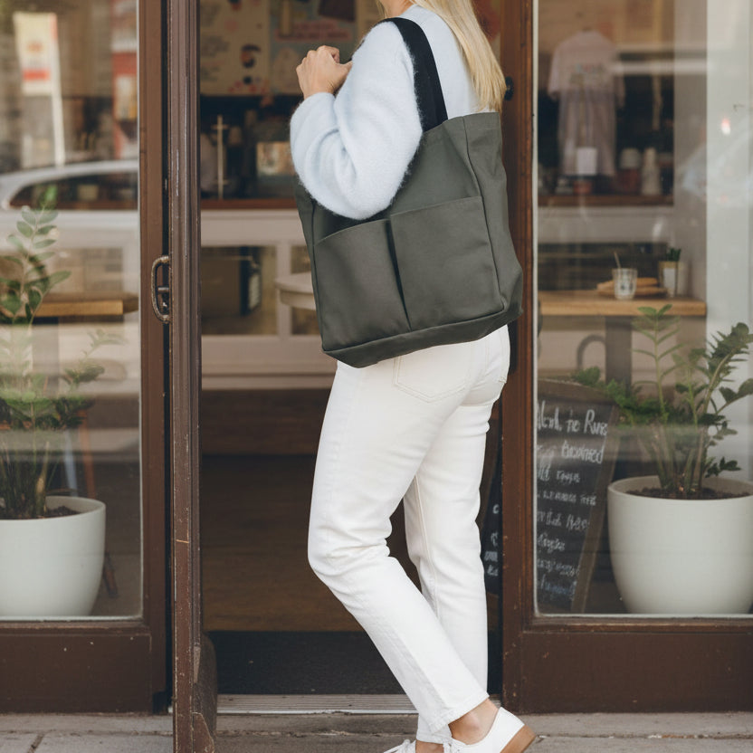 Woman wearing an olive green canvas tote bag on her shoulder while exiting a plant shop
