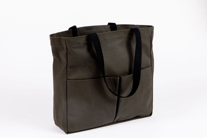 Olive canvas tote bag with two front pockets and black webbing handles, shown at a three-quarter angle