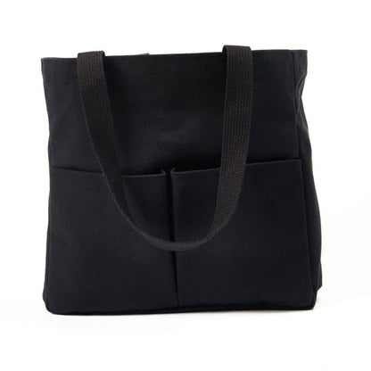 Black canvas tote bag with two wide shoulder straps and two front utility pockets, shown against a white background
