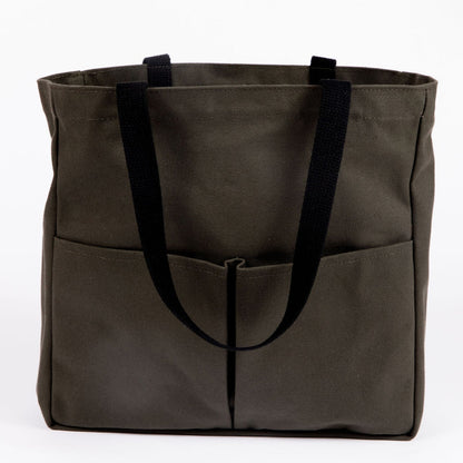 Olive green canvas tote bag with black webbing handles and two front utility pockets, shown on a white background
