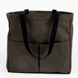 Olive green canvas tote bag with black webbing handles and two front utility pockets, shown on a white background
