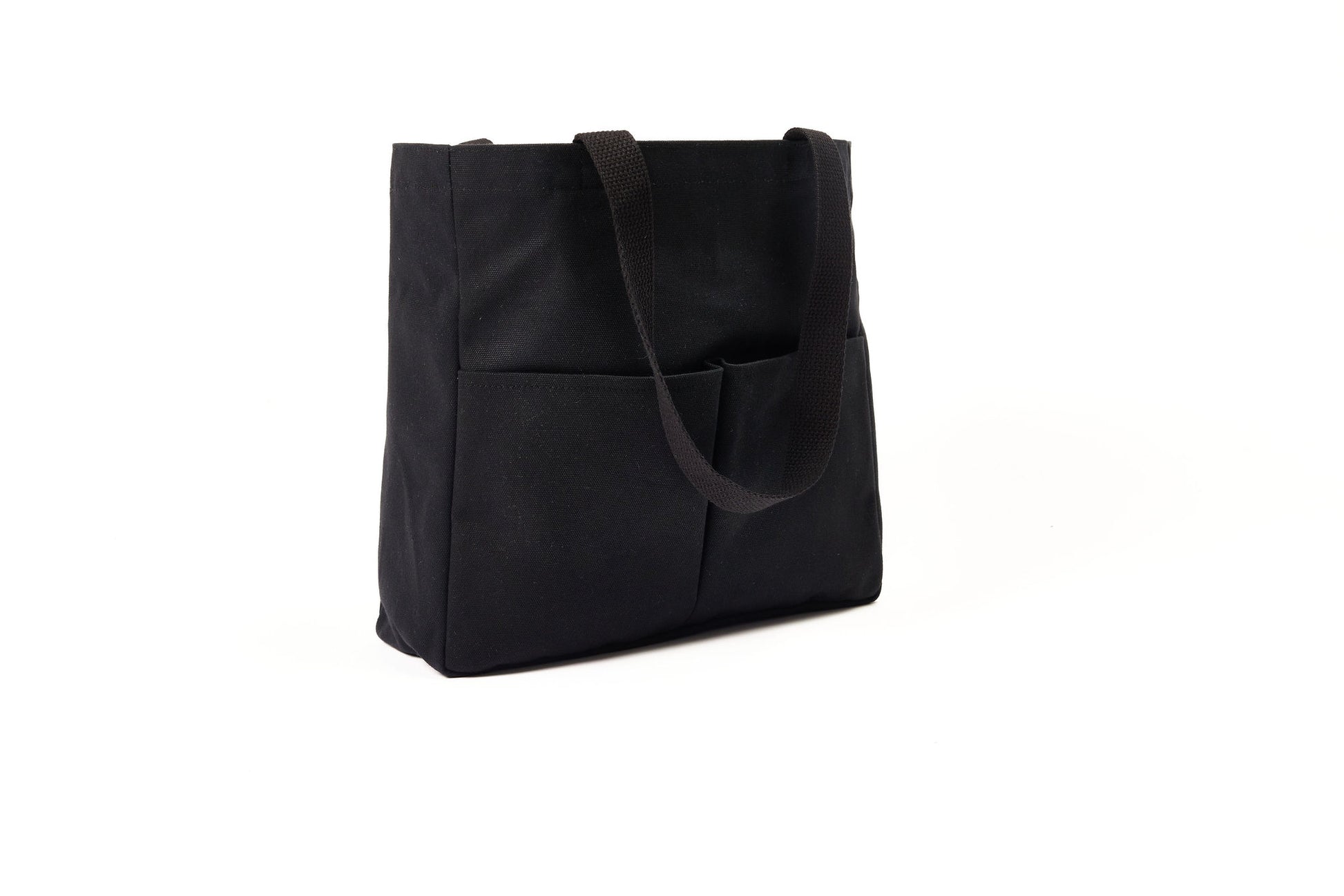 Black canvas Utility Carryall tote with two shoulder straps and front pockets, photographed on a white background
