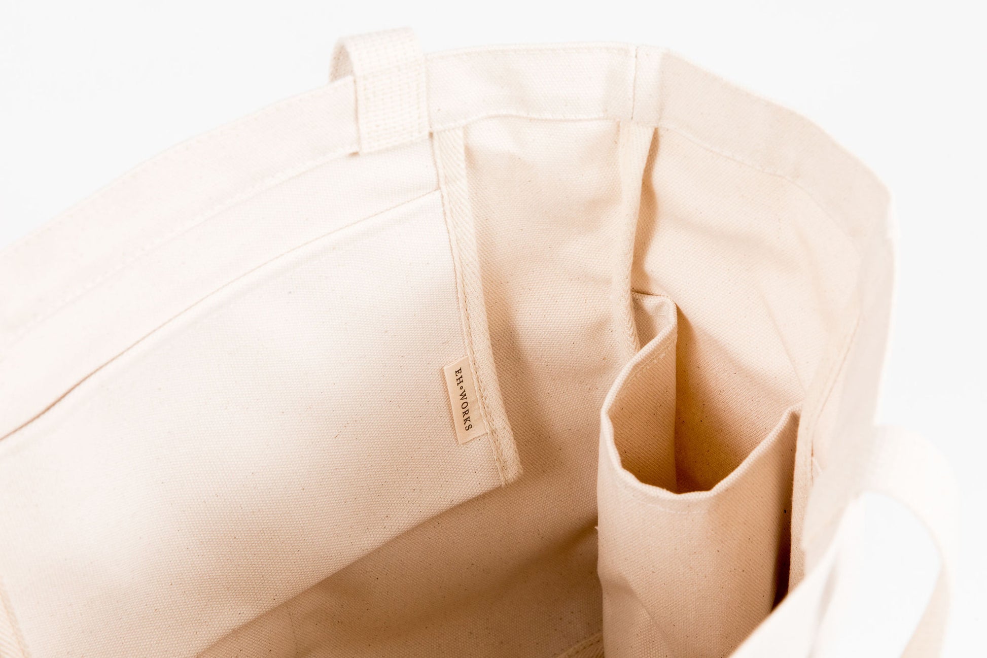  Close-up of a natural canvas Utility Carryall tote showing the EH·Works brand label and front pocket