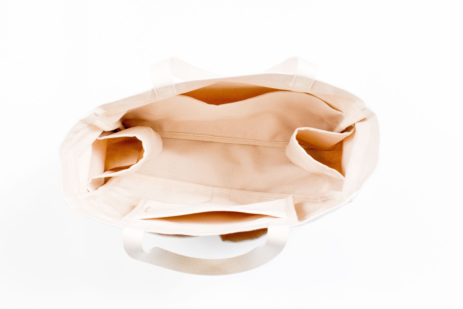 Top-down view inside an empty natural canvas Utility Carryall tote, showing interior pockets
