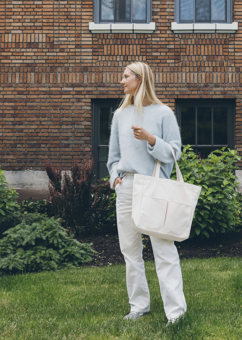 Woman holding a natural canvas Utility Carryall tote in front of a brick building