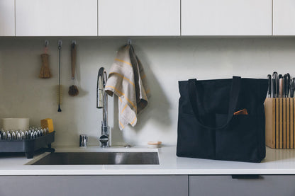 Canvas Utility Carryall tote in black on a kitchen counter, with a wooden tool tucked in the front pocket