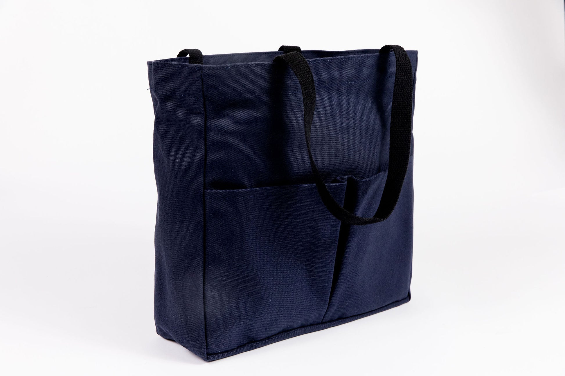 Canvas Utility Carryall tote in navy, three-quarter view showing front pockets and black webbing handles