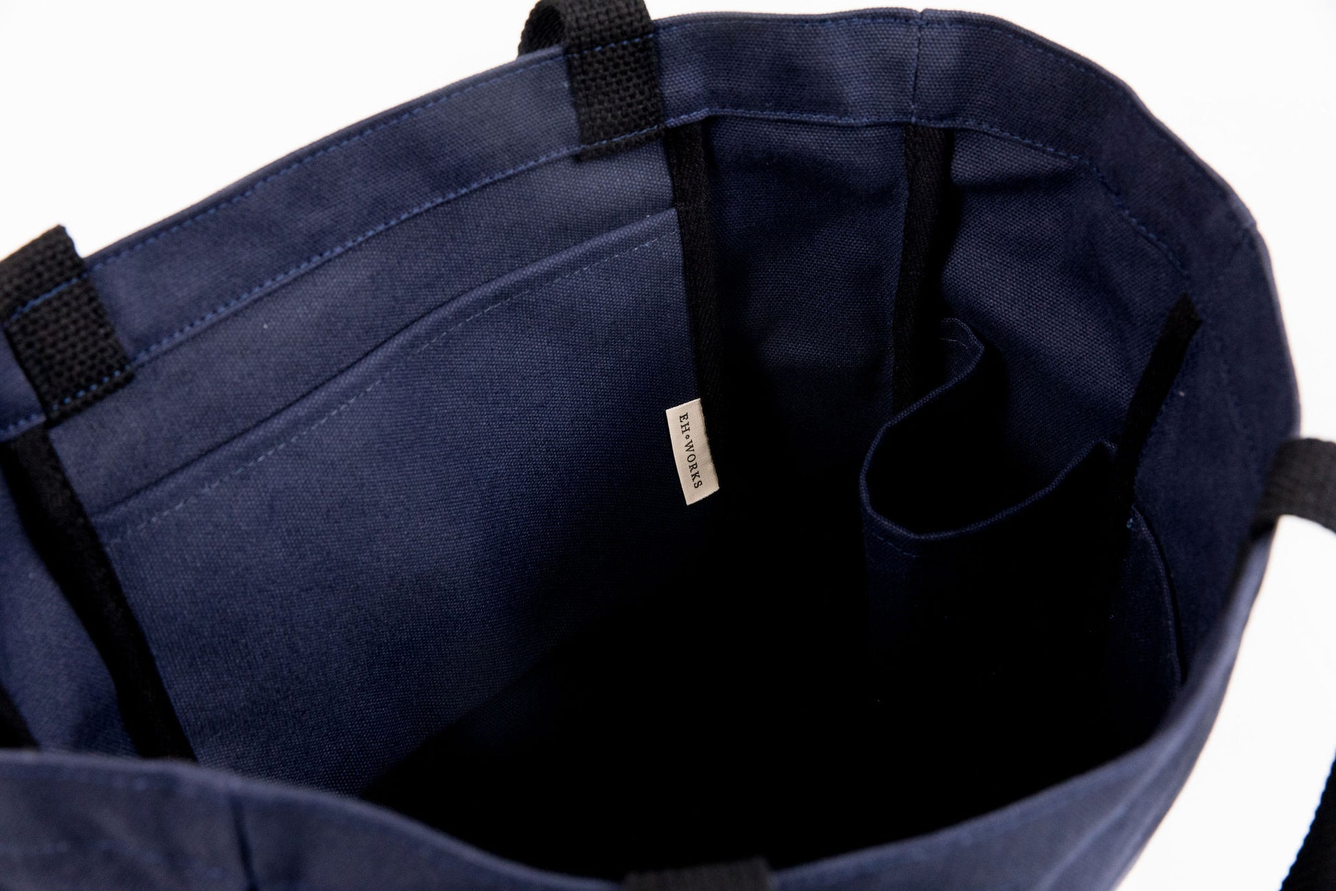 Close-up of a navy canvas tote's interior, showing the EH·Works label tag and stitched pocket dividers