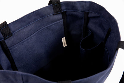 Close-up of a navy canvas tote's interior, showing the EH·Works label tag and stitched pocket dividers