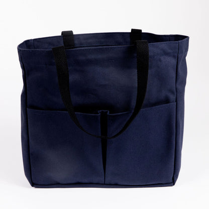 Canvas Utility Carryall tote in navy, with front pockets and black webbing handles, shown on a white background
