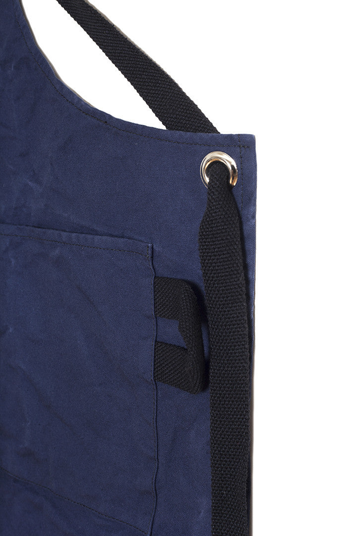 Close-up of a navy canvas apron showing the adjustable strap, metal grommet, and side pocket