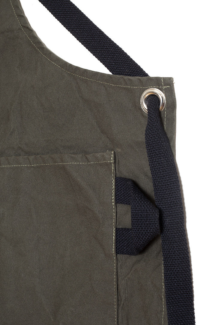 Close-up of a pine canvas apron showing the adjustable strap, metal grommet, and side pocket