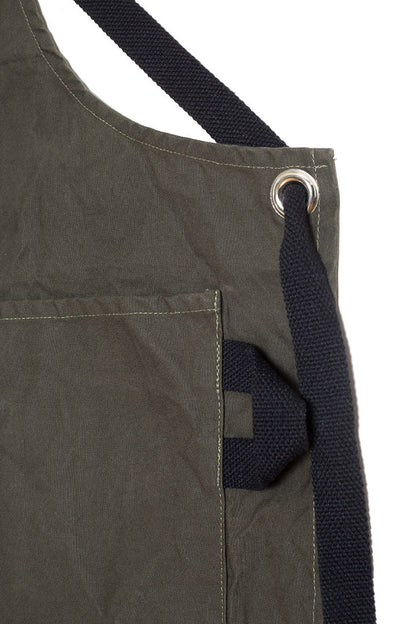 Close-up of a pine canvas apron showing the adjustable strap, metal grommet, and side pocket