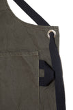 Close-up of a pine canvas apron showing the adjustable strap, metal grommet, and side pocket