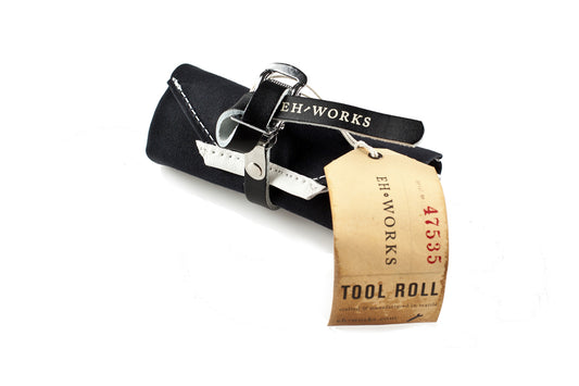 Black waxed canvas Sojourner tool roll with black leather strap, rolled up with an EH·Works "Tool Roll" tag