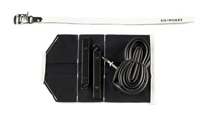 Open black canvas Sojourner tool roll with white leather trim, showing tire levers and a spare tube in the pockets
