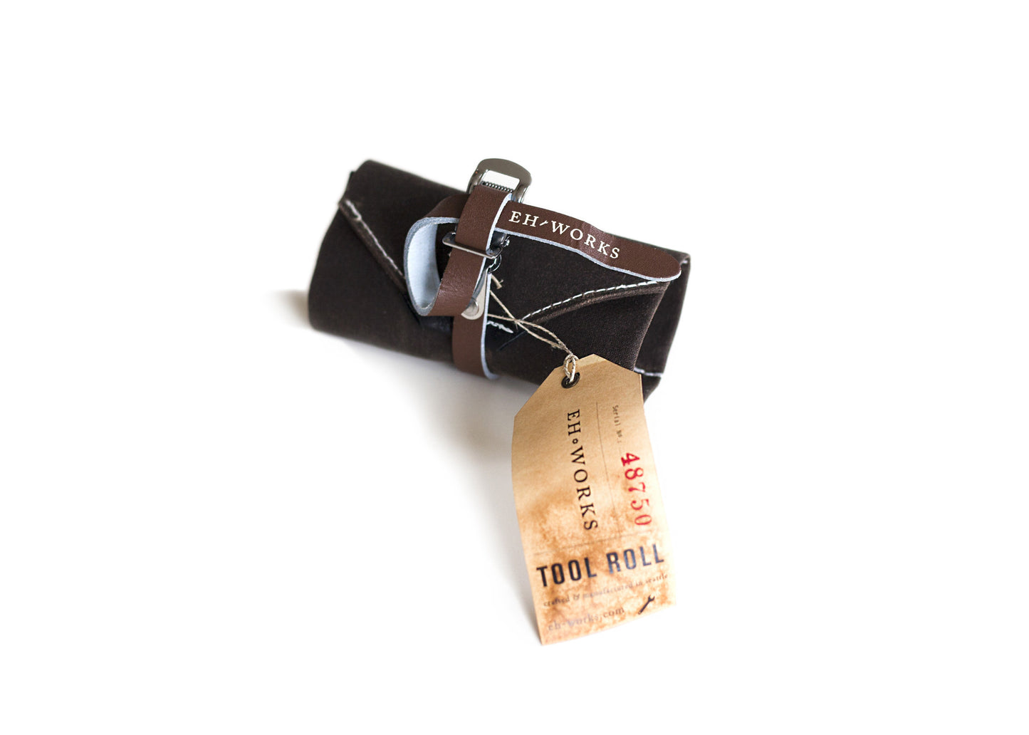 Sojourner tool roll in dark canvas with a saddle brown leather strap and light blue interior lining, rolled up with an EH·Works "Tool Roll" tag